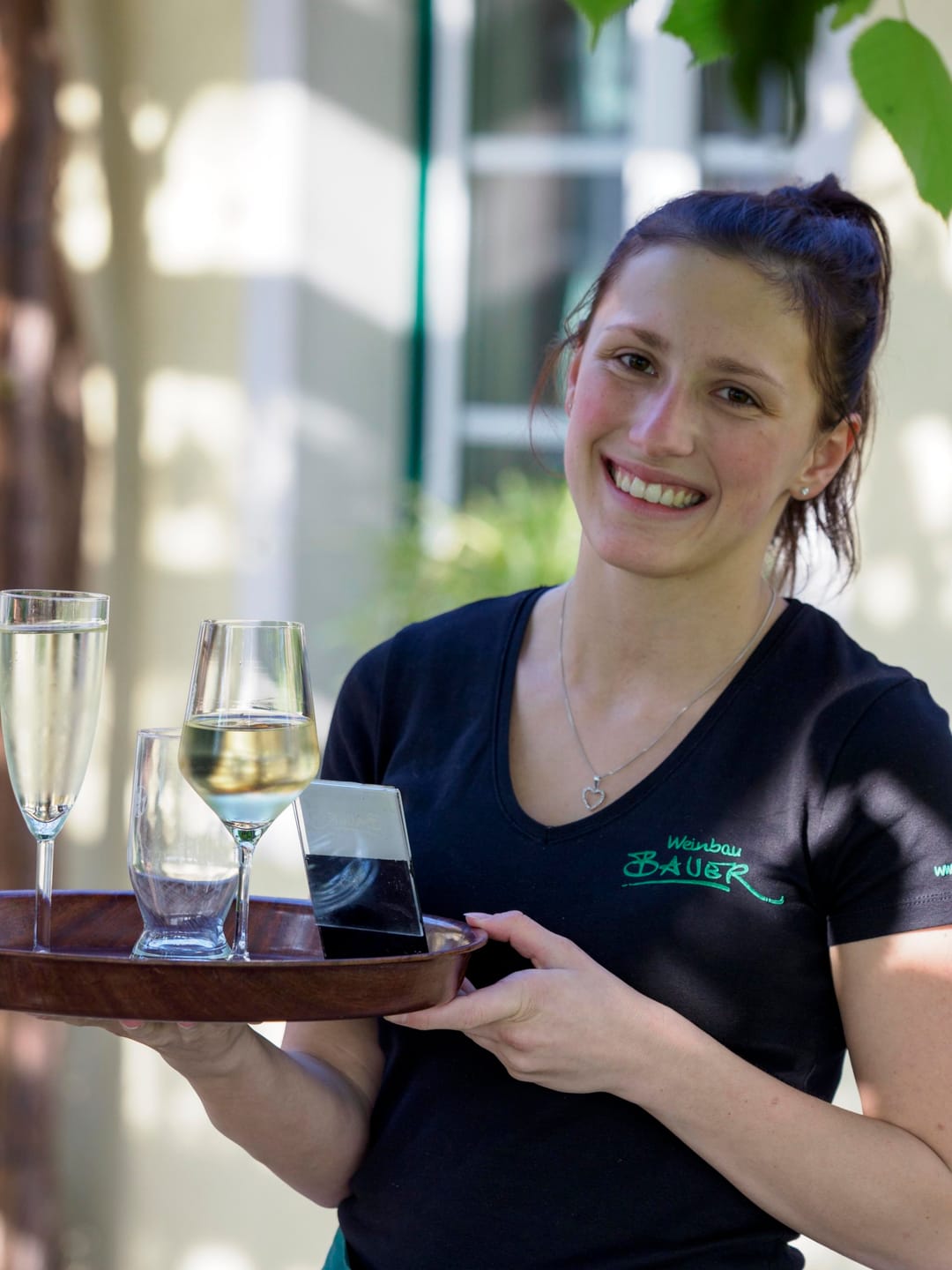 Mitarbeiterin mit Weinbau-Bauer-Shirt trägt ein Tablett mit gefüllten Weingläsern