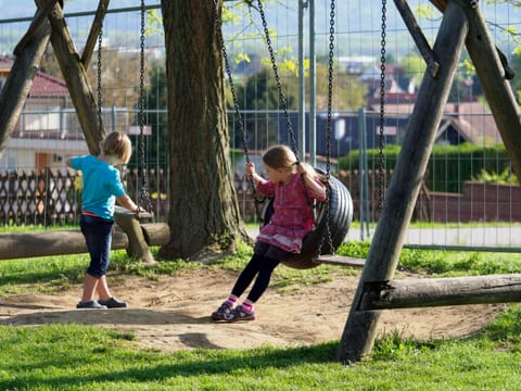 Kinder auf einem Spielplatz mit Schaukel neben dem Gastgarten